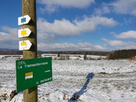 The Transardennaise sign on a post in the middle of snowy fields. - Everything you need to know to prepare your hike in the Ardennes